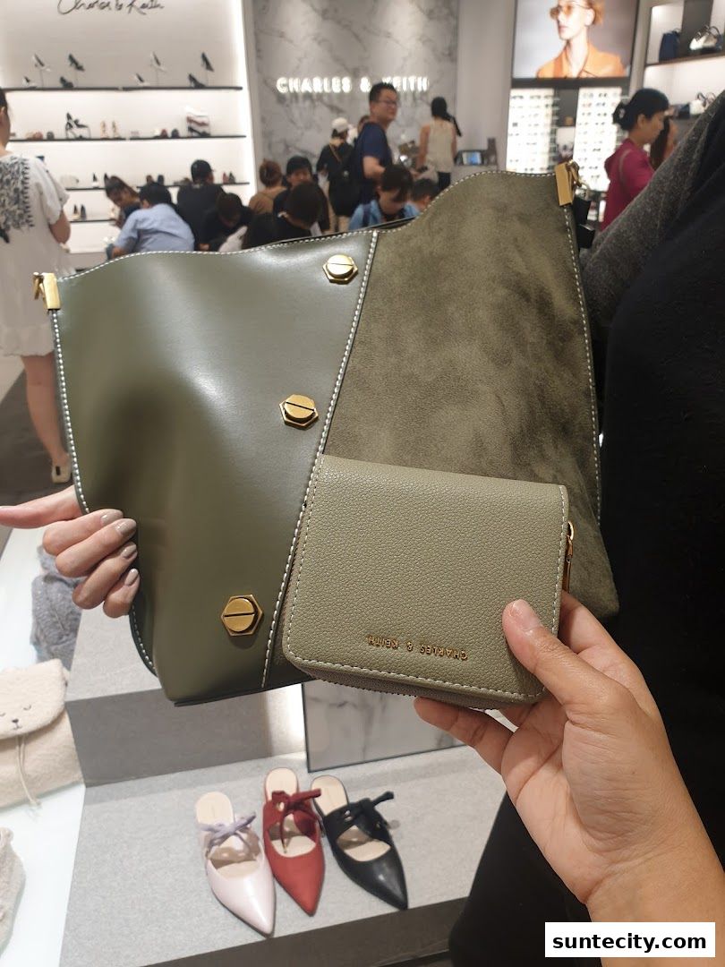 A person holds a green Charles & Keith wallet and bag in front of a display of shoes.