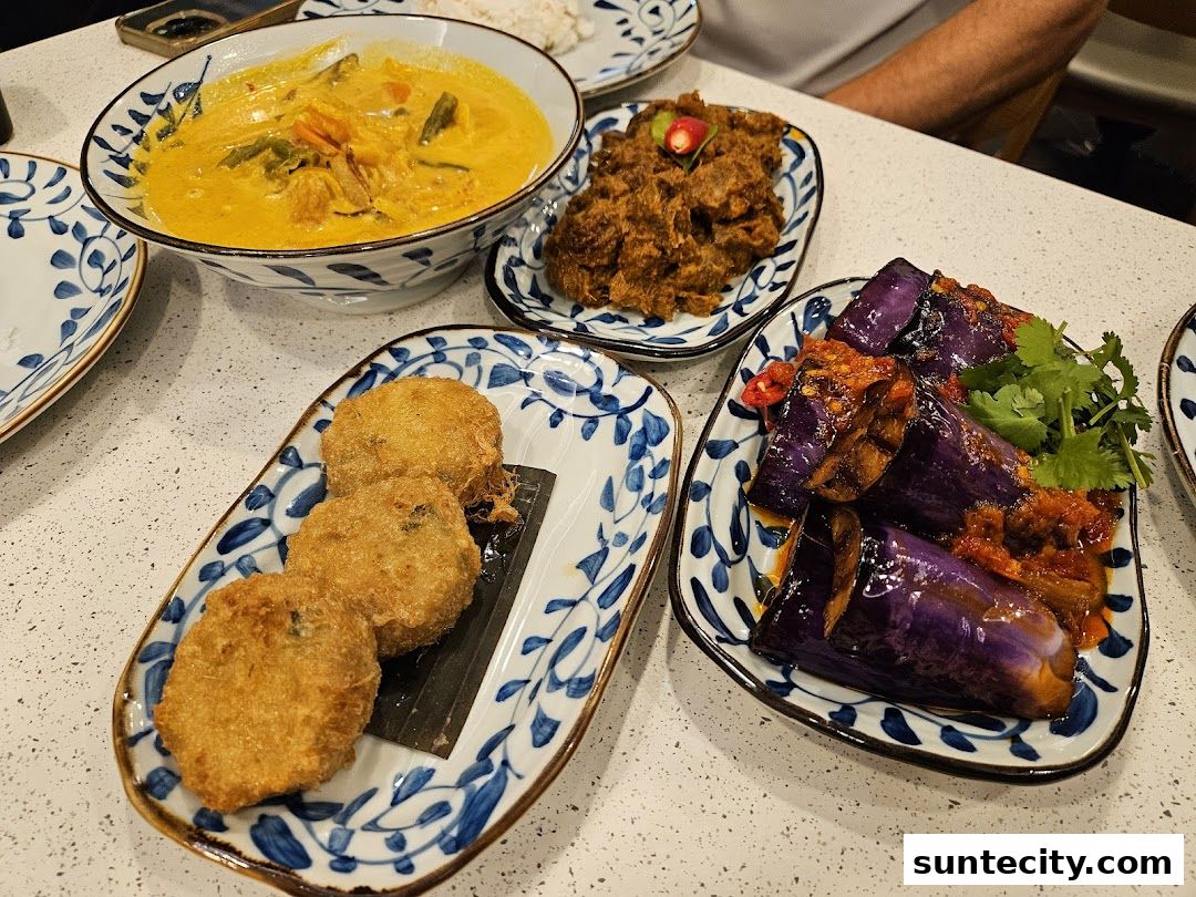 A table laden with delicious Indonesian dishes, including curry, rendang, fried patties, and eggplant.