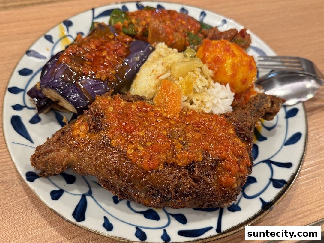 A plate of Indonesian food with fried chicken, rice, eggplant, and egg.