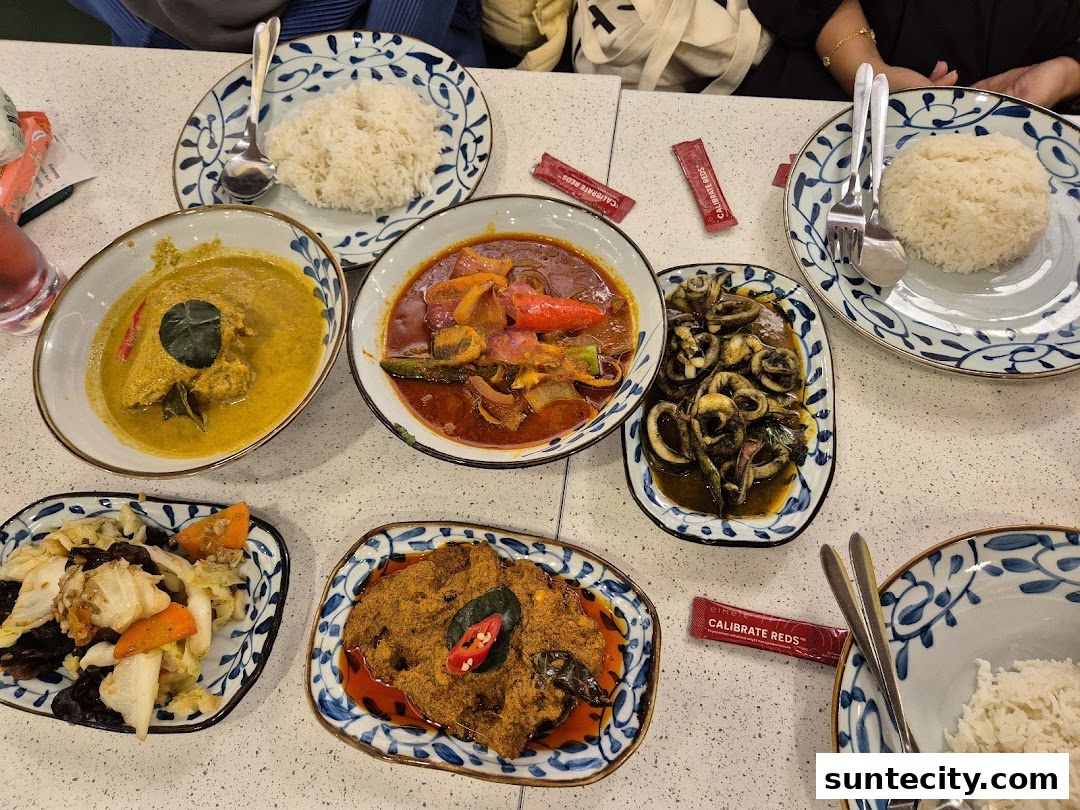 A table laden with various Indonesian dishes, including rice, curry, and stir-fried squid.