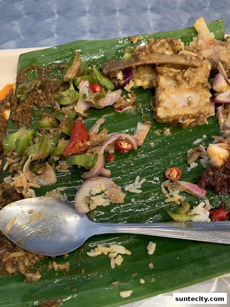 A close-up of a plate of Indonesian food served on a banana leaf with a spoon.
