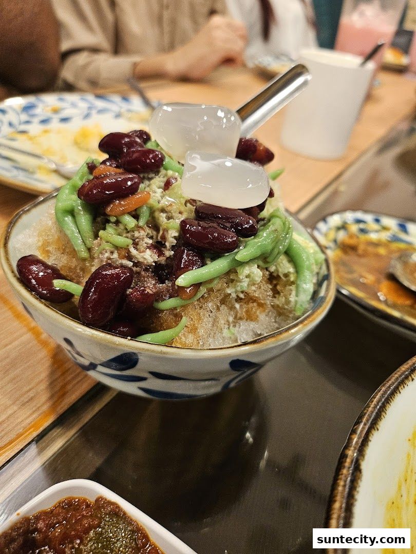 A close-up of a refreshing dessert with shaved ice, red beans, and green jelly.