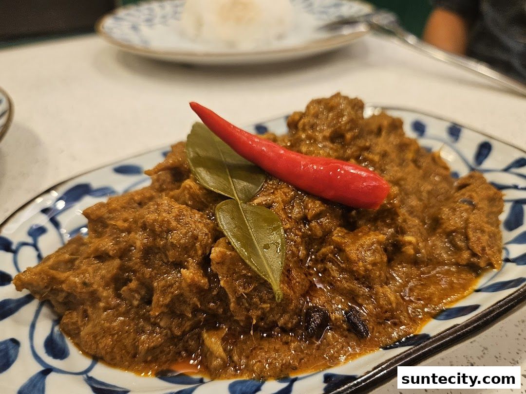 A close-up of a flavorful Indonesian beef rendang dish garnished with a red chili and kaffir lime leaves.