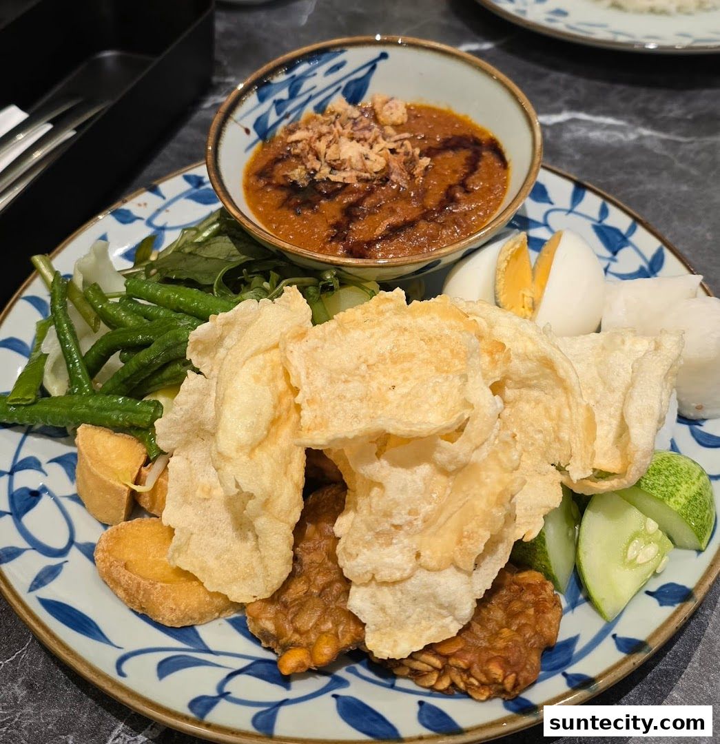 A plate of Indonesian food with peanut sauce, vegetables, tempeh, tofu, egg, and crackers.