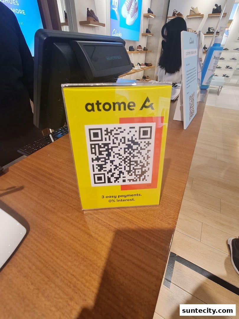 A yellow sign with a QR code and 'atome' logo is displayed at the counter of a Clarks shoe store.