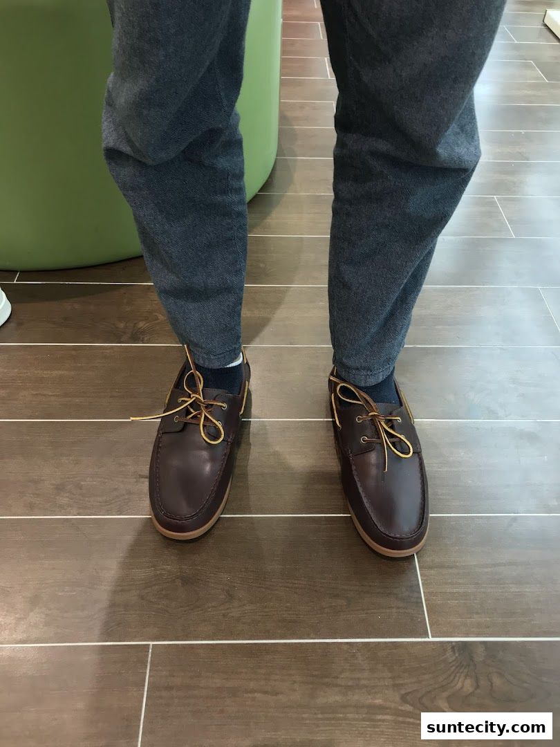 A person wearing brown leather boat shoes with yellow laces and dark grey pants.