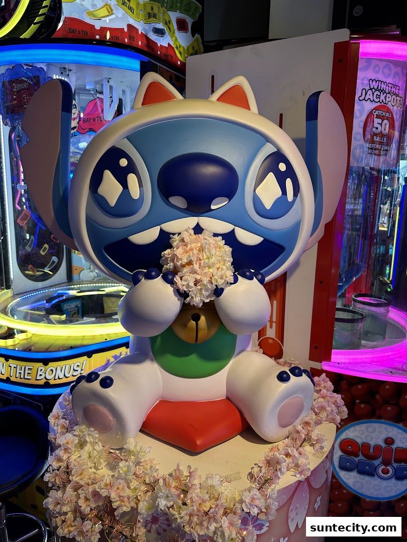 A large Stitch character statue decorated with flowers in front of arcade games.