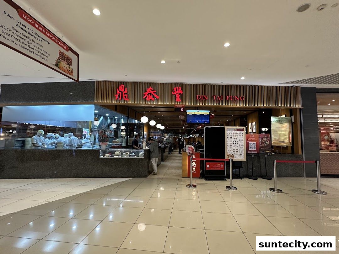 The exterior of Din Tai Fung restaurant with chefs visible in the kitchen and a queue management system.