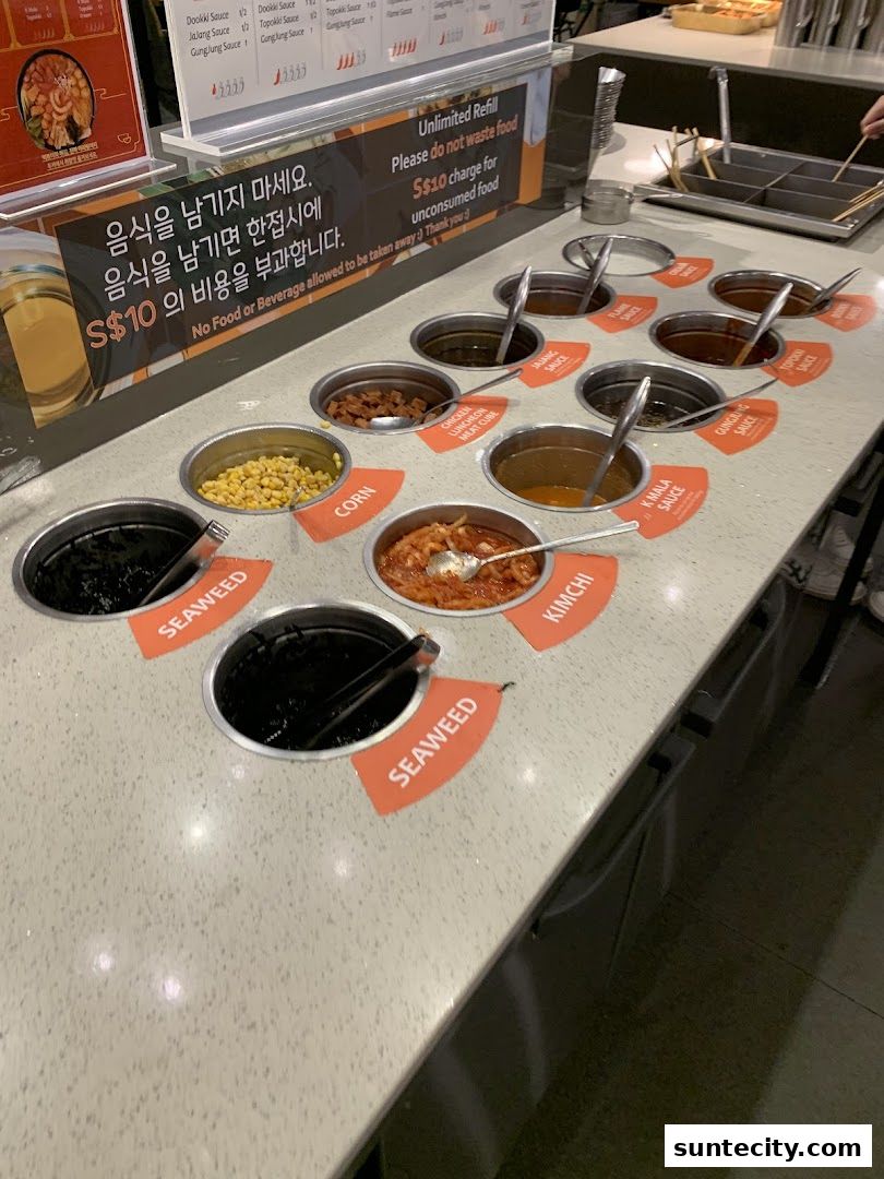 A variety of sauces and ingredients are displayed in metal containers at a food establishment.