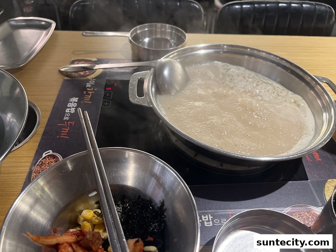A bubbling pot of soup with various ingredients in bowls on a table.