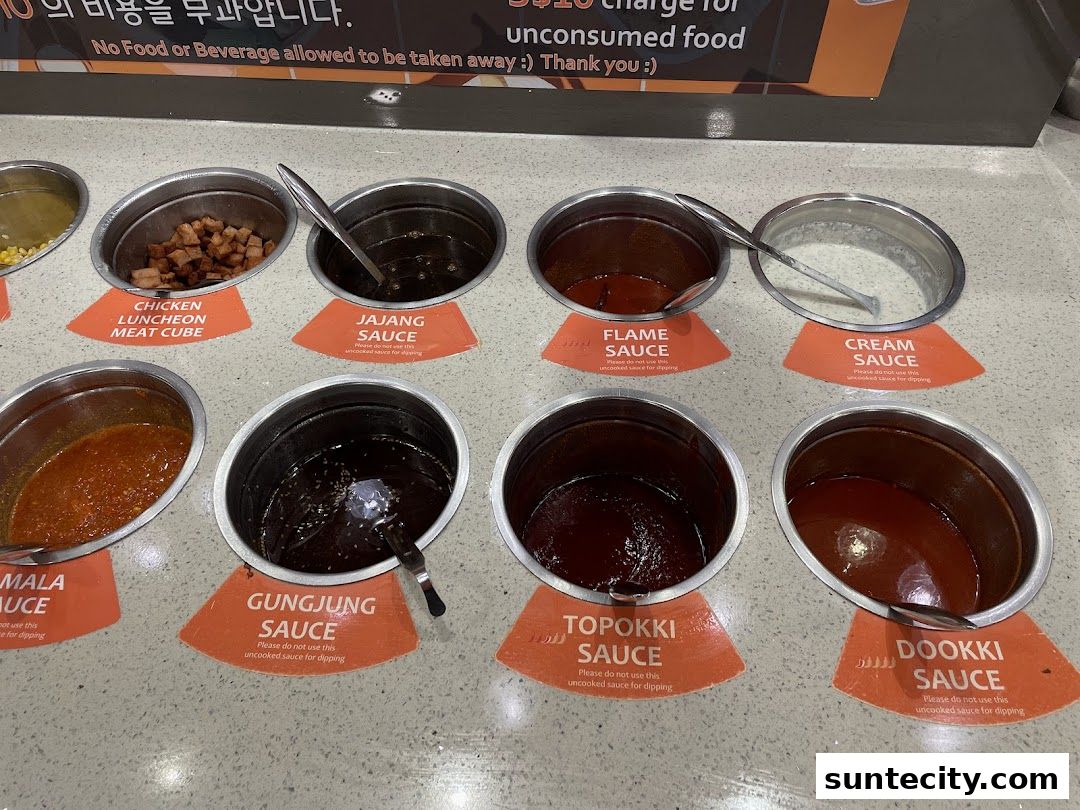 A variety of sauces and ingredients are displayed in metal containers for customers to choose from.
