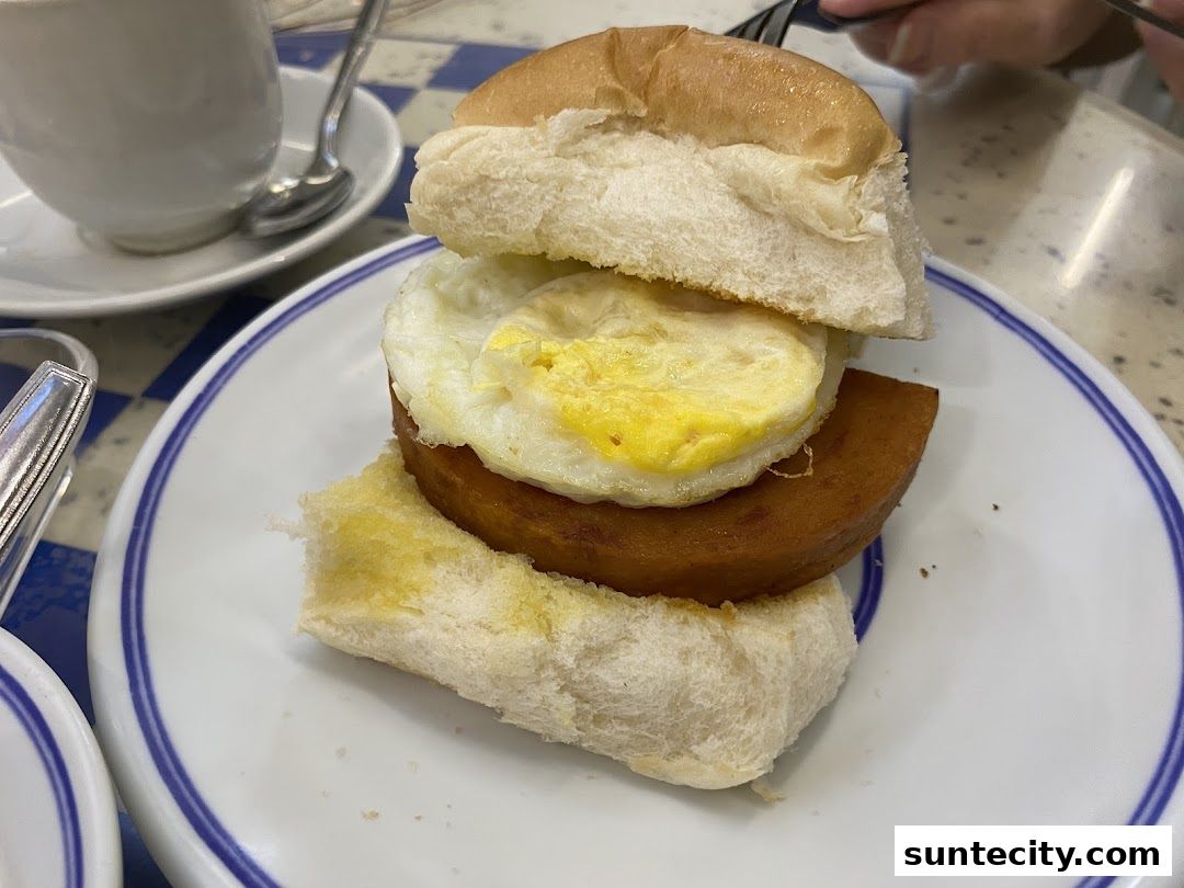 A close-up of a breakfast sandwich with fried egg and spam on a bun.