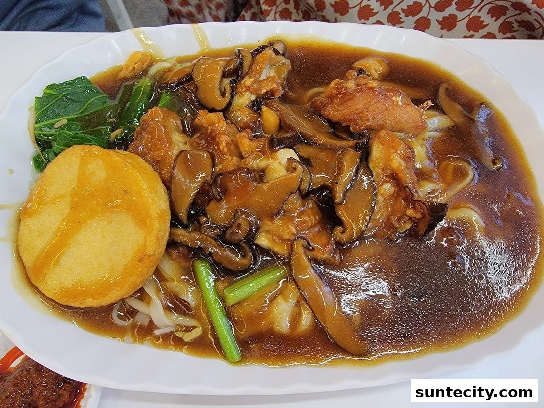 A plate of noodles with mushrooms, vegetables, and fried tofu in a savory sauce.