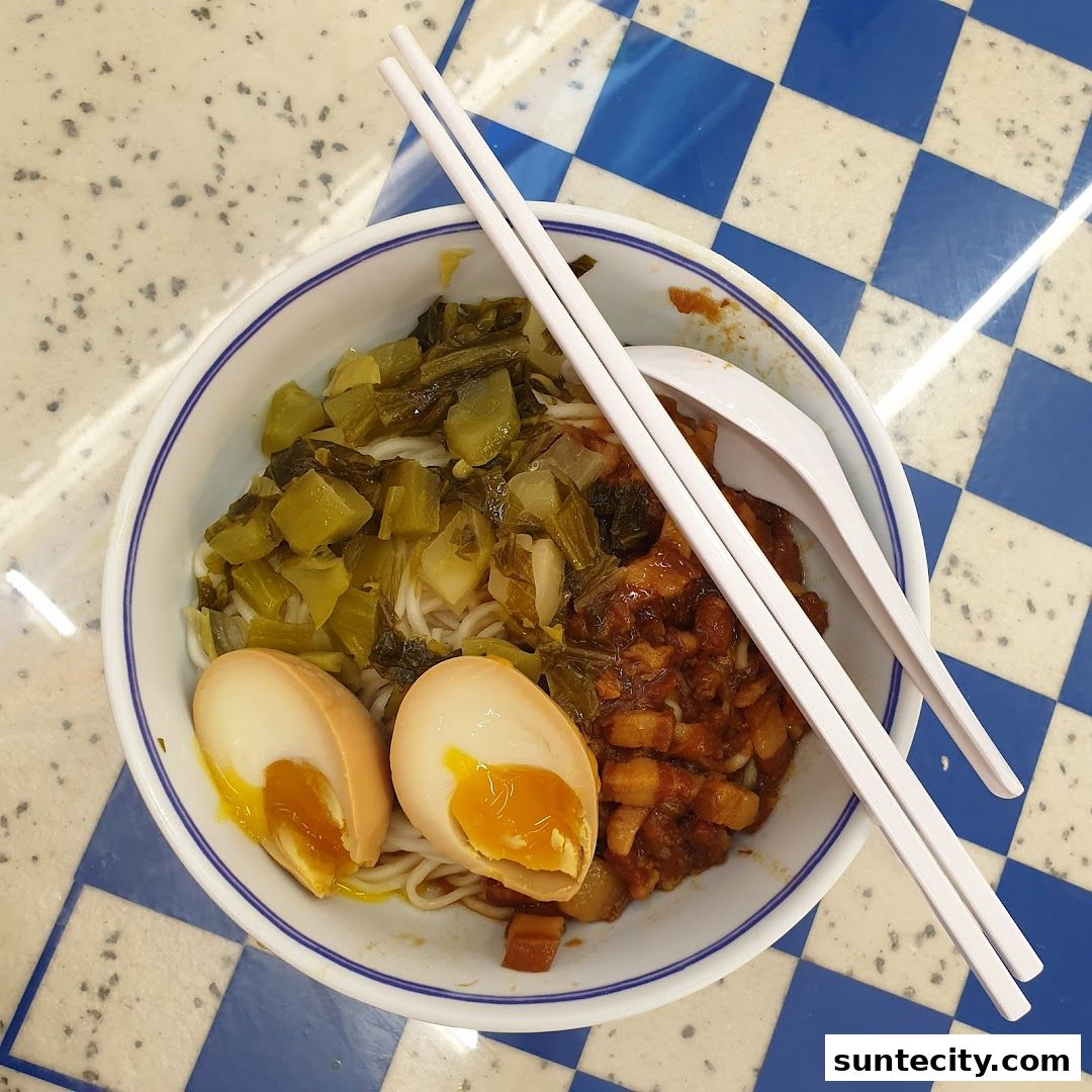 A bowl of noodles with braised pork, pickled vegetables, and a soft-boiled egg.
