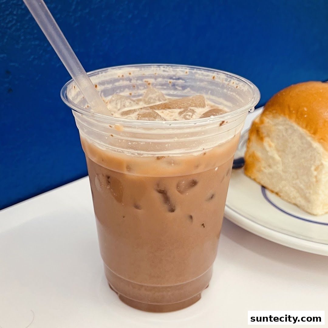 A close-up of an iced coffee with a straw and a pastry on a plate.