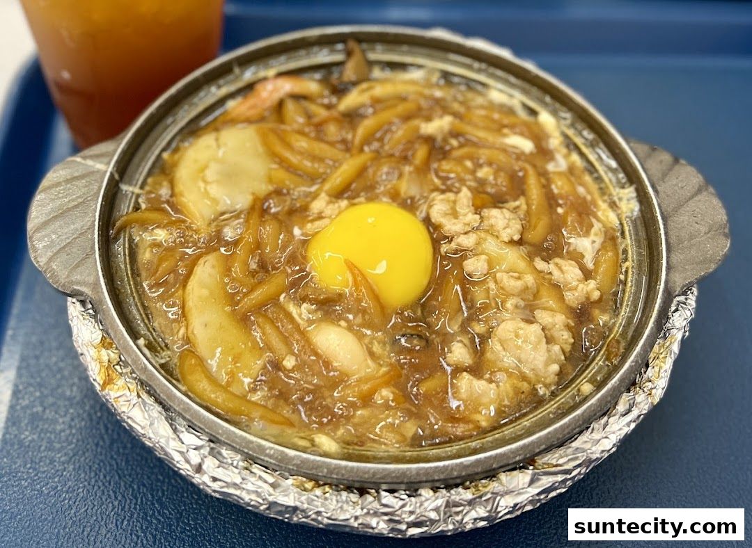 A close-up of a hot pot dish with noodles, egg, and meat, served with a drink.