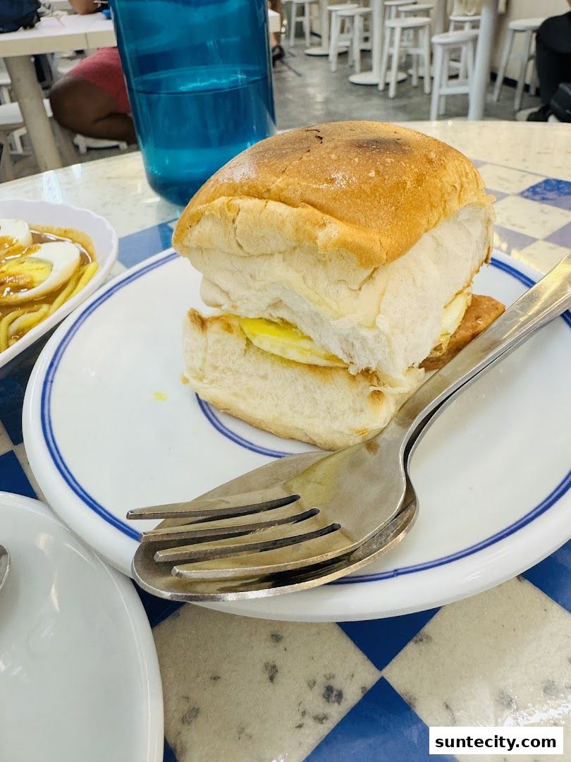 A close-up of a burger with a fried egg and a side dish of noodles and boiled eggs.