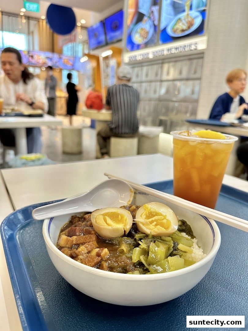 A close-up of a bowl of braised pork rice with a side of pickled vegetables and a drink.