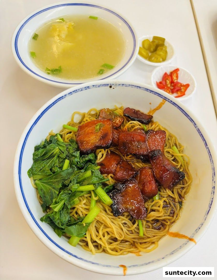 A bowl of noodles with char siu, greens, and a side of soup and condiments.
