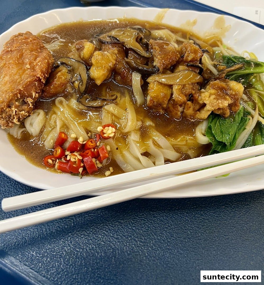 A close-up of a delicious noodle dish with fried chicken, mushrooms, and chili.
