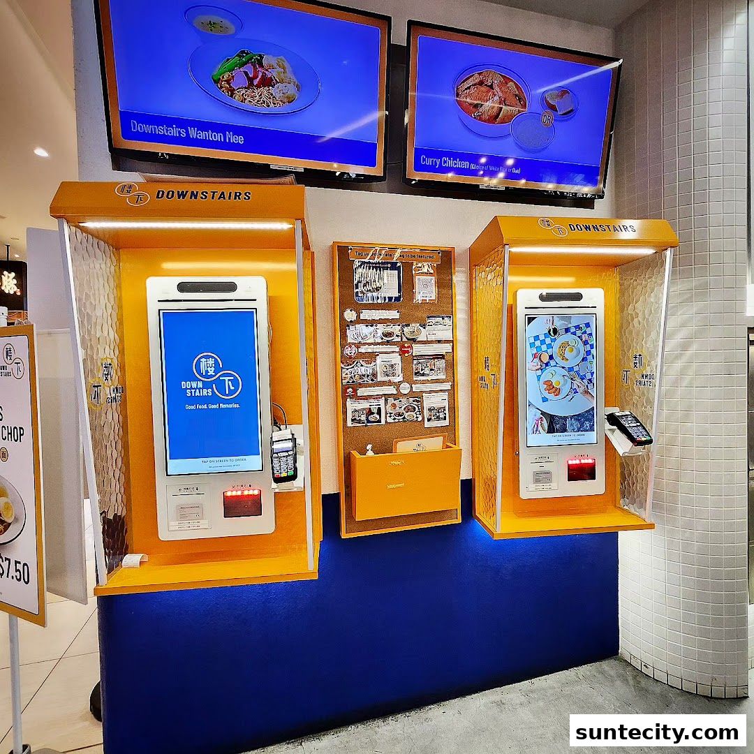 Two digital ordering kiosks and a corkboard display for a food establishment called Downstairs.