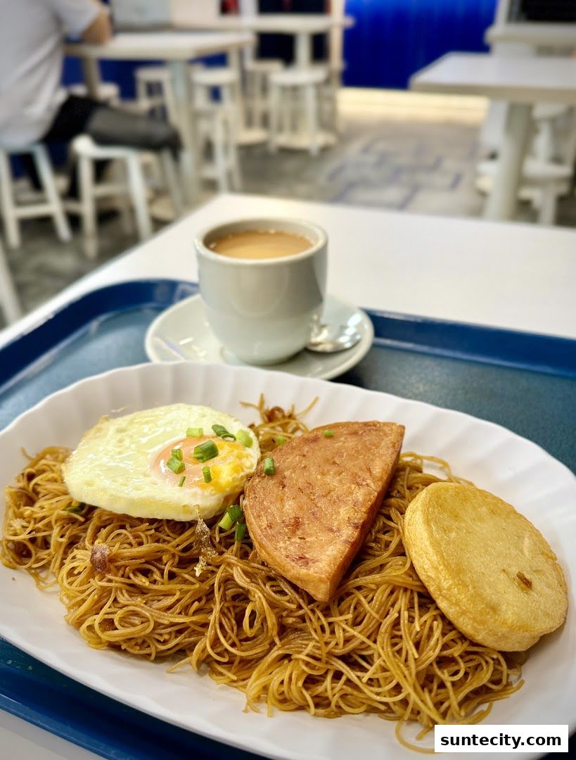 A plate of fried noodles with fried egg, spam, and fish cake, served with a cup of coffee.