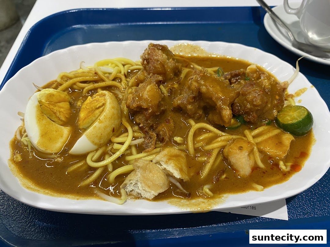 A plate of noodles with curry sauce, fried chicken, boiled egg, and lime.
