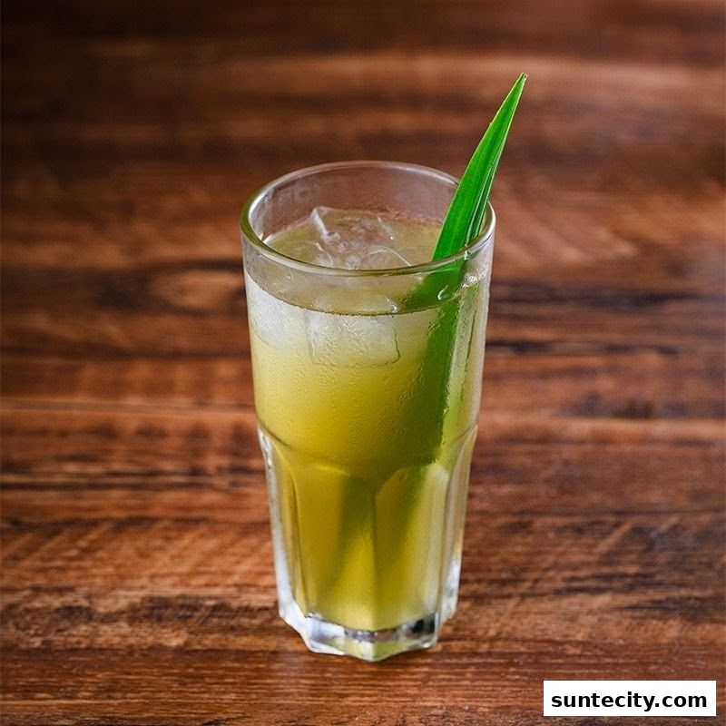 A refreshing green beverage with ice and a pandan leaf garnish on a wooden table.