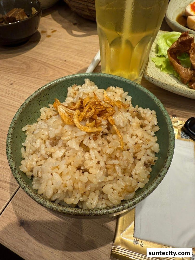 A bowl of fragrant rice topped with crispy fried shallots, served with a drink and side dishes.