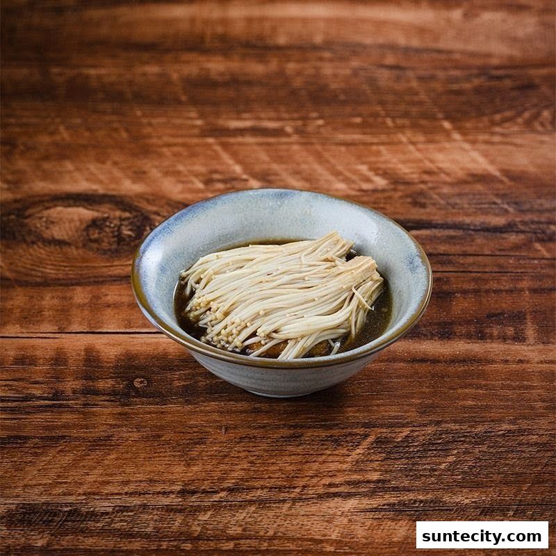A bowl of enoki mushrooms in broth on a wooden table.