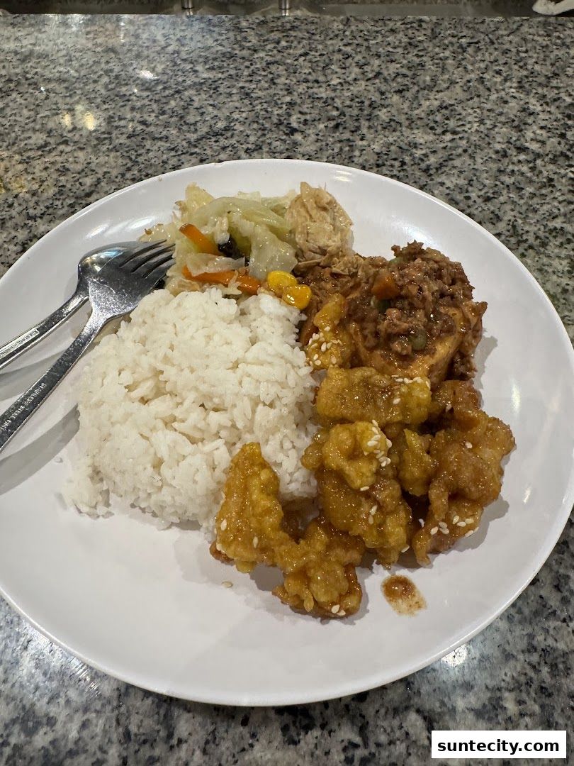 A white plate filled with rice, stir-fried vegetables, and crispy sesame chicken.
