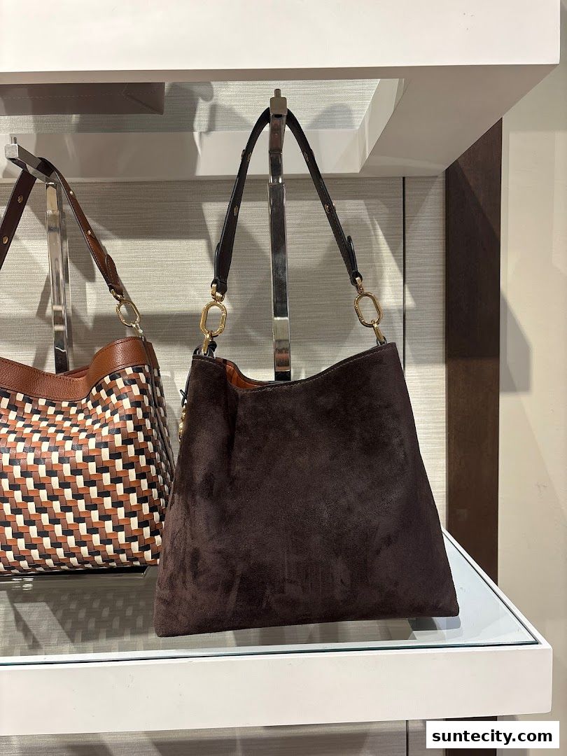 A dark brown suede handbag is displayed on a shelf next to another patterned handbag.