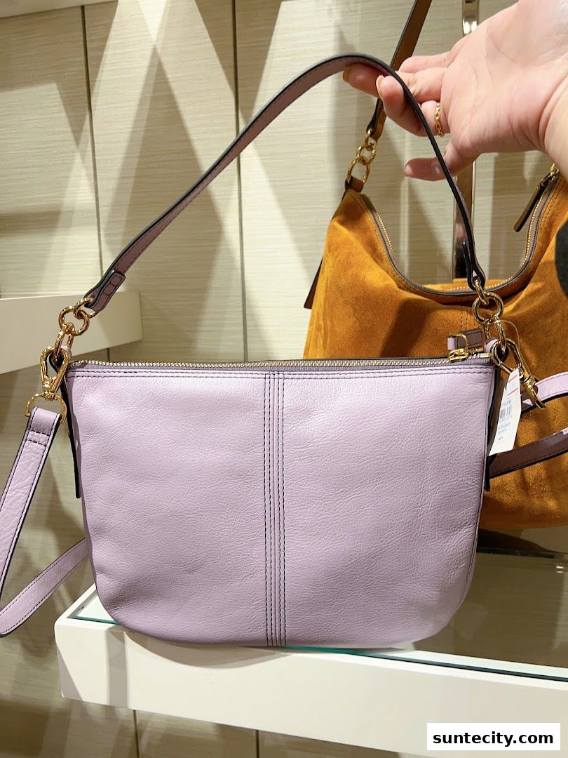 A person holds a light purple leather handbag with a chain strap in a retail store.