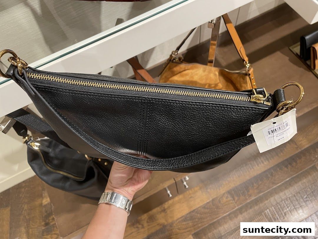 A hand holds a black leather crossbody bag with gold hardware at Fossil.