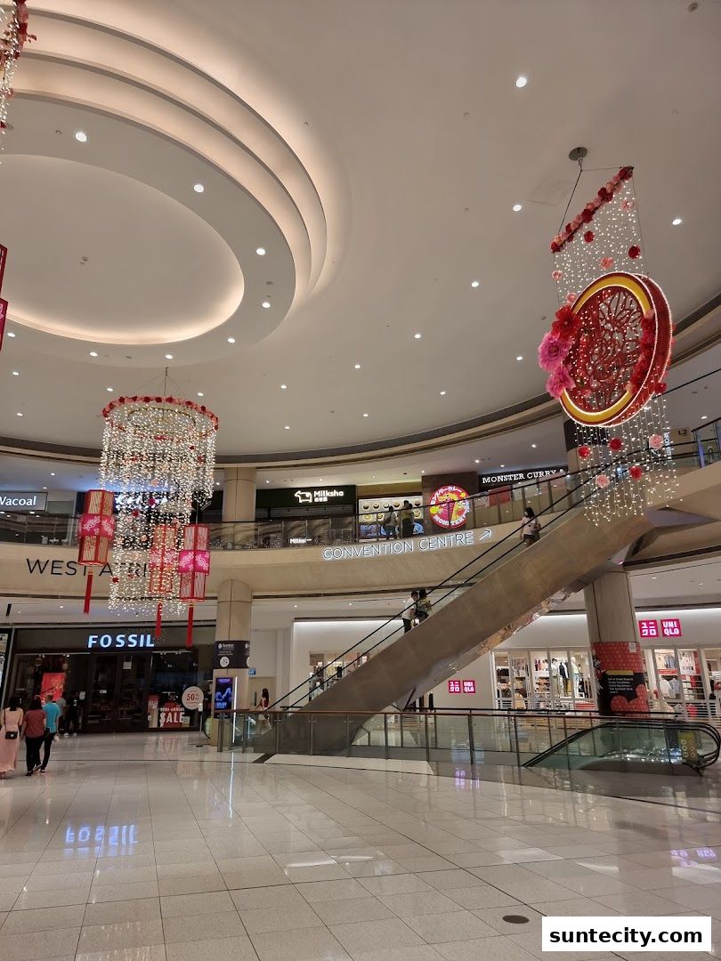Interior view of a shopping mall with escalators, shops, and festive decorations.
