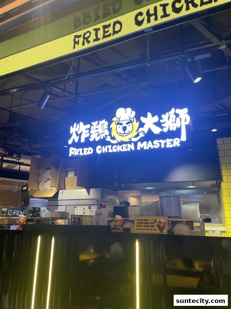 The illuminated sign for Fried Chicken Master, featuring a lion mascot, above a counter.