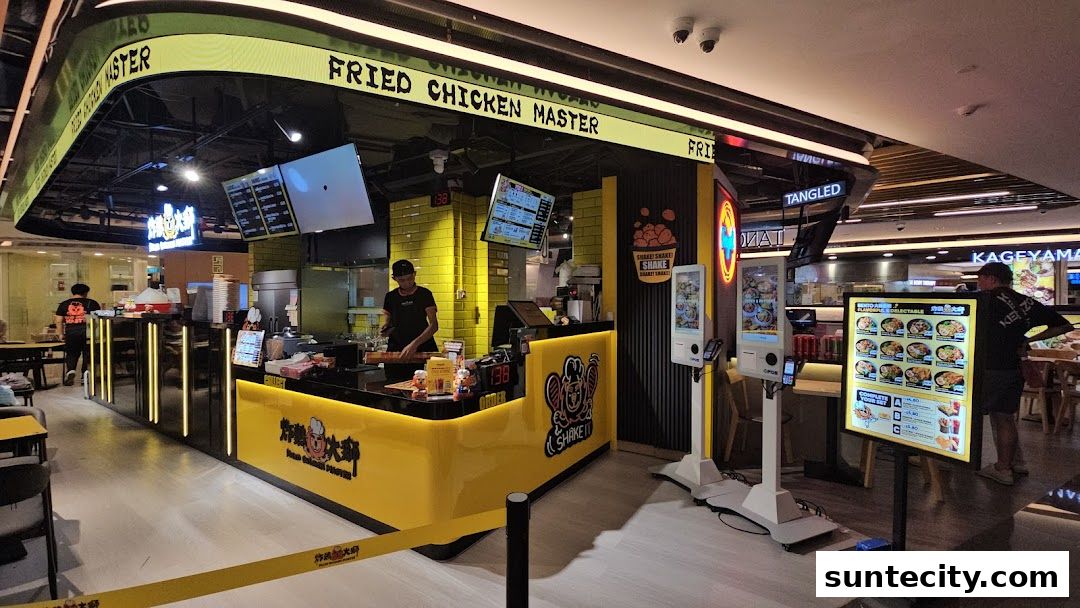 A bright yellow fried chicken stall with digital menus and a staff member serving customers.