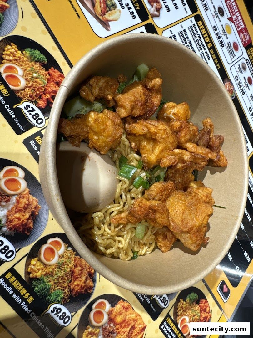 A bowl of noodles with fried chicken and a boiled egg, with menu items visible in the background.