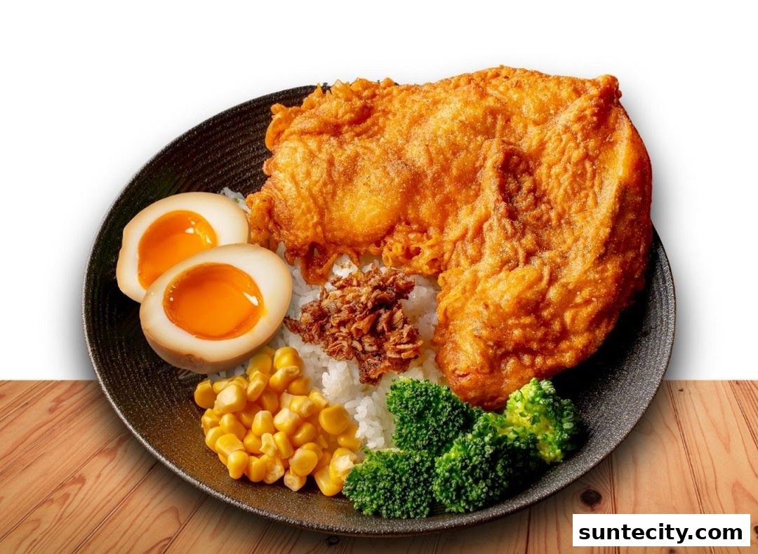 A delicious plate of fried chicken with rice, soft-boiled eggs, corn, broccoli, and crispy shallots.