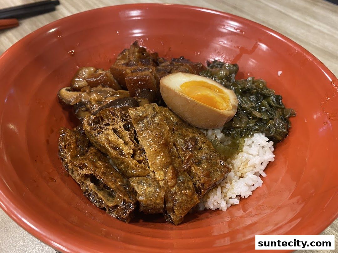 A close-up of a red bowl filled with rice, braised pork, mushrooms, a braised egg, and pickled vegetables.