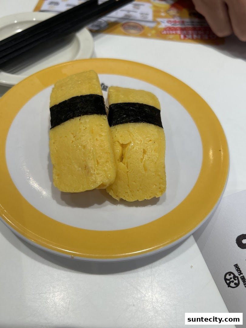Two pieces of tamagoyaki sushi on a plate with chopsticks in the background.