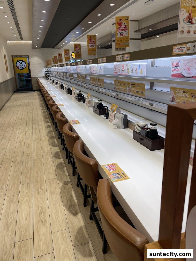Interior of a Genki Sushi restaurant with a conveyor belt sushi system and empty seats.