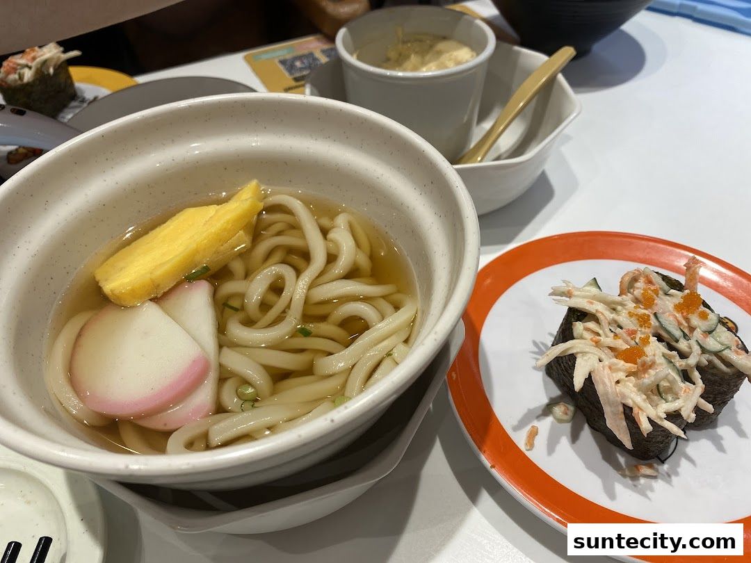 A close-up of a bowl of udon noodles and two pieces of sushi on a plate.