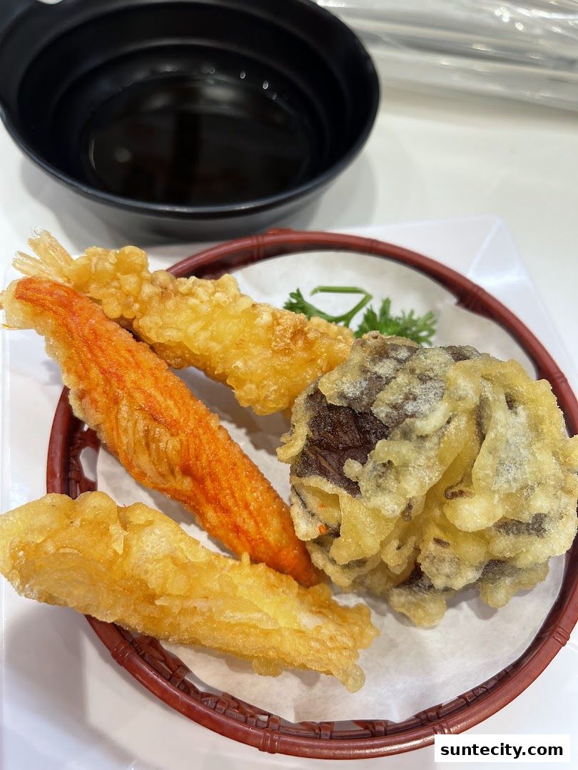 A plate of assorted tempura, including crab stick, fish, and mushroom, with a dipping sauce.