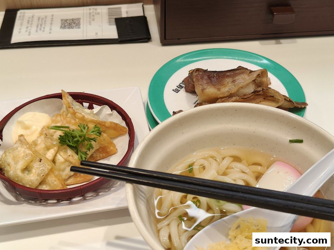 A close-up of Japanese food including udon noodles, fried dumplings, and grilled meat.