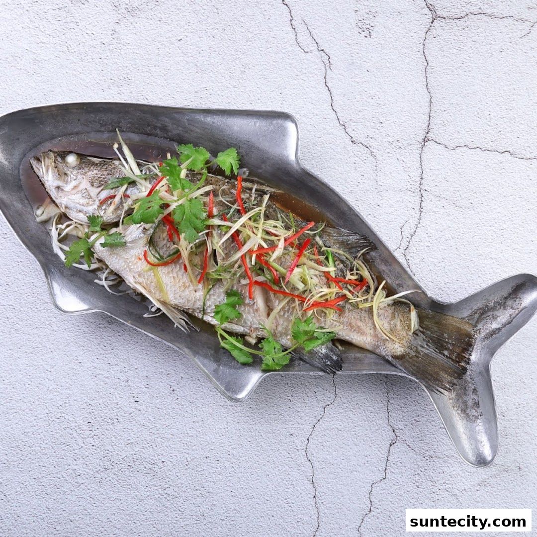 A whole steamed fish, garnished with ginger, scallions, and chili, served on a fish-shaped platter.