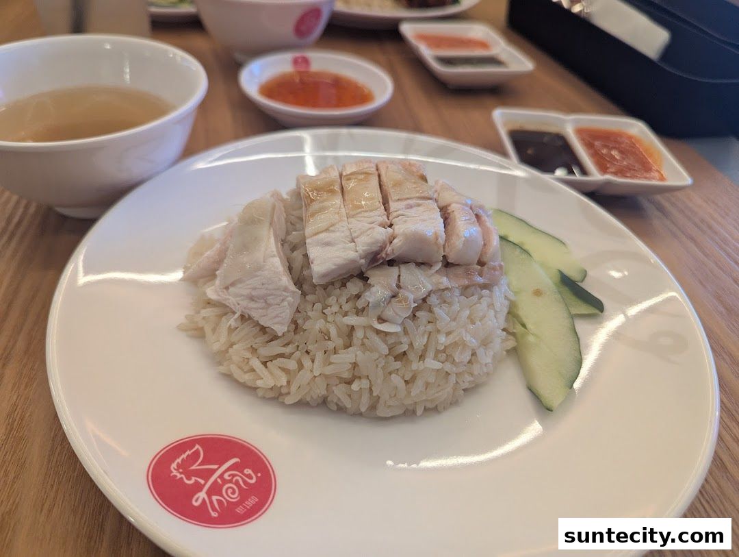 A plate of delicious chicken rice with cucumber slices and a side of soup.