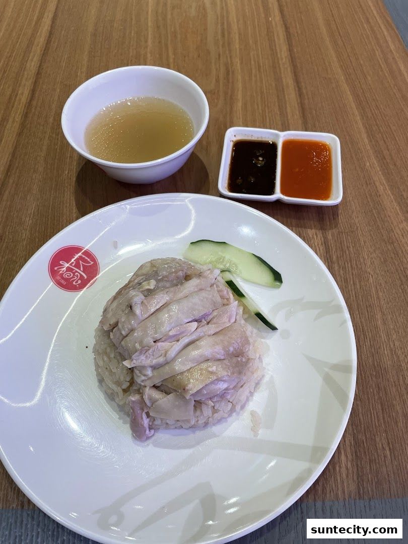 A plate of chicken rice with soup and dipping sauces on a wooden table.