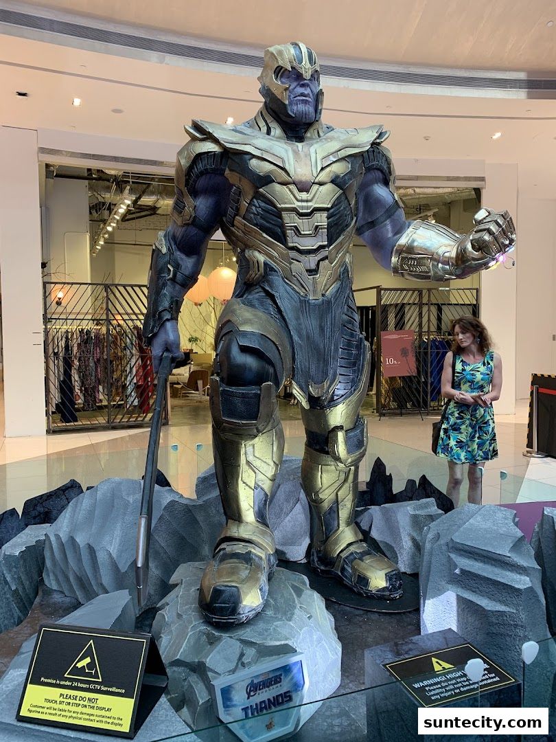 A large Thanos statue is displayed in a shopping mall with a woman standing nearby.