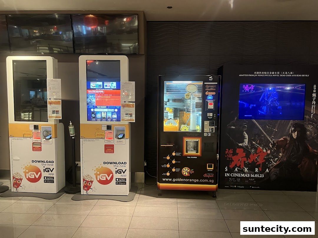 Self-service kiosks, a vending machine, and movie posters are displayed in a cinema lobby.